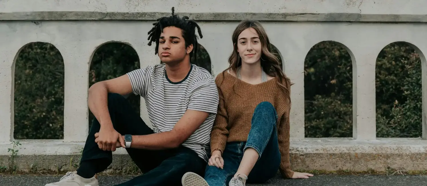 get-the-care-you-need A teenage boy and girl sitting next to each other on a bridge